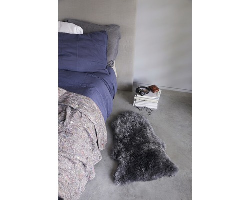 Schlafzimmer mit Bett, Bücherstapel, Kopfhörern und Schaffellteppich.