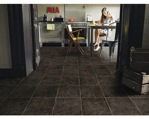 Moderne Küche mit dunklem Fliesenboden und einer Frau am Esstisch.