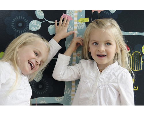 Zwei Kinder an einer Wachstumstabelle vor einer floralen Wandtapete