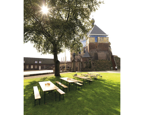 Biergartenszene mit Holztischen und -bänken auf einer Rasenfläche vor einem Schlossgebäude
