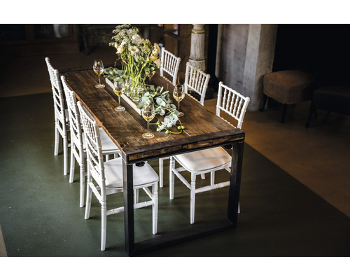 Esstisch mit Holzplatte, Metallgestell und weißen Stühlen, dekoriert mit Blumen und Weingläsern.