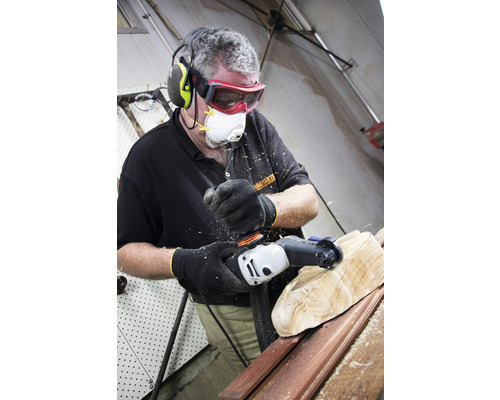 Mann mit Gehörschutz, Schutzbrille und Atemschutzmaske bearbeitet Holz mit einem Elektrowerkzeug.