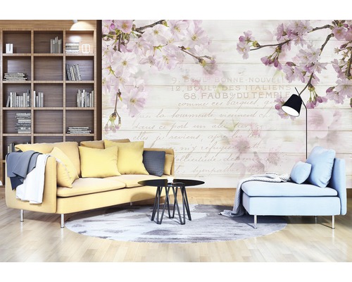 Wohnzimmer mit Sofa, Sessel, Tisch und Bücherregal vor einer Wandtapete mit Blütenmotiven