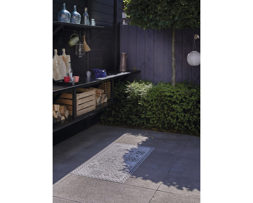 Außenbereich mit Holzkohlegrill, Holzlager und dekorativem Teppich auf Steinfliesen