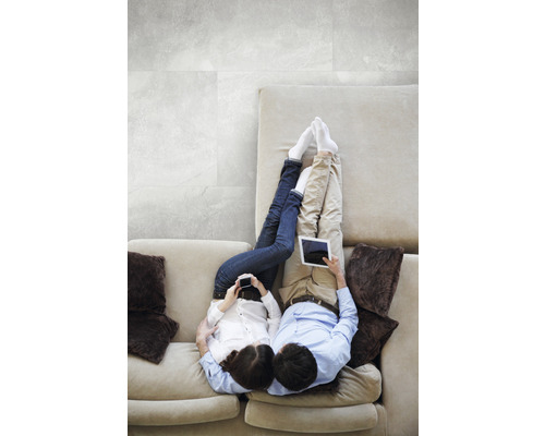 Ein Paar entspannt sich auf einem Sofa mit elektronischen Geräten vor einem gefliesten Hintergrund.