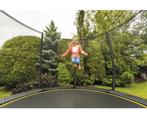 Mädchen springt auf einem Gartentrampolin mit Sicherheitsnetz vor Bäumen