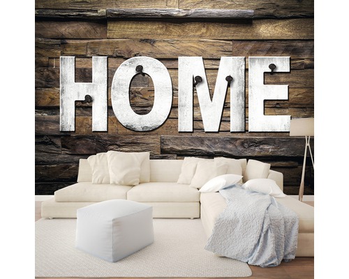 Wohnzimmer mit Sofa, Hocker und Wanddekoration mit dem Schriftzug HOME auf Holzpaneelen.