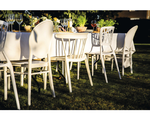 Szene mit Gartenmöbeln: Tisch mit weißer Tischdecke und Stühlen auf einer Rasenfläche.