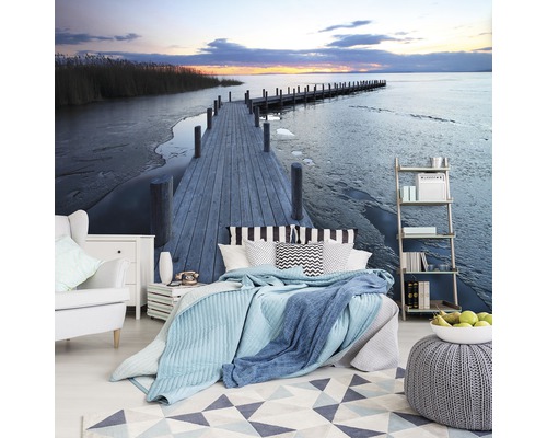 Wohnraum mit Fototapete, die einen Steg am See bei Sonnenuntergang zeigt.