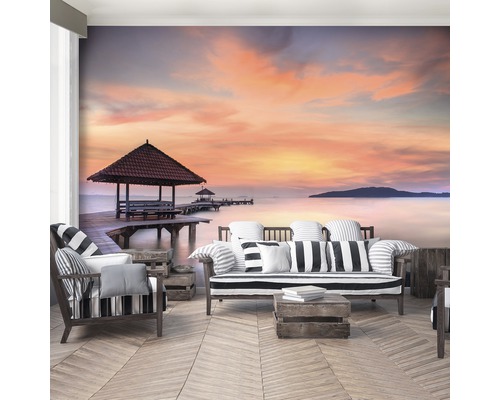 Wohnraum mit Fototapete eines Sonnenuntergangs am Meer mit Holzsteg und Pavillon
