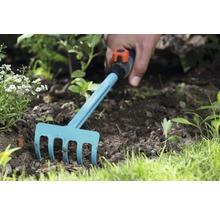 Gartenharke im Einsatz in einem Beet mit Erde und Pflanzen.