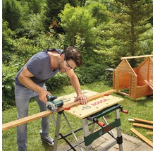 Mann sägt Holz mit einer Handkreissäge auf einer Bosch Werkbank im Garten.