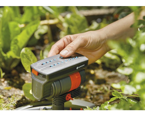 Eine Hand bedient einen Gardena Regner im Garten.