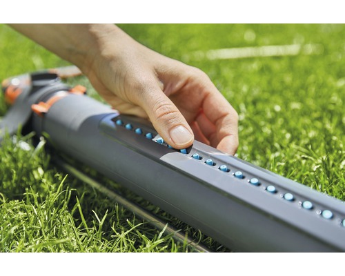 Eine Person bedient einen Rasensprenger im Garten.