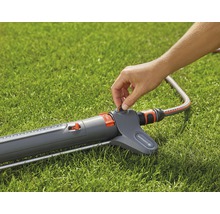 Eine Person bedient einen Gartensprenger auf einem Rasen.