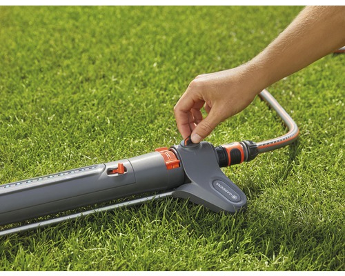 Eine Person bedient einen Gartensprenger auf einem Rasen.