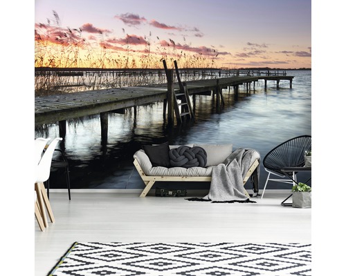 Wandbild mit einem Steg auf einem See bei Sonnenuntergang in einem hellen Raum