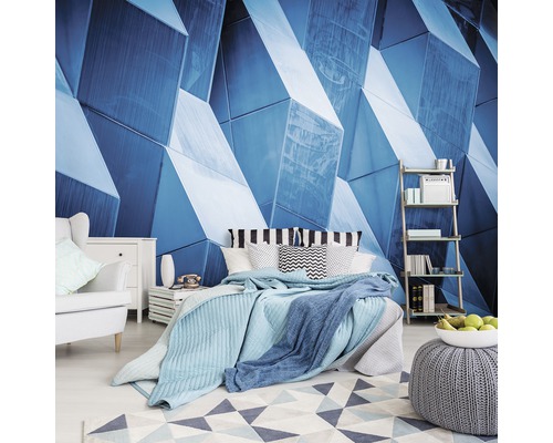 Schlafzimmer mit blauem geometrischen Wandbild, Bett, Sessel und Regal