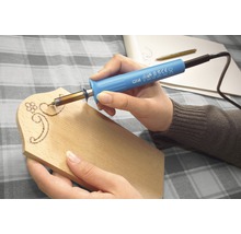 Person arbeitet mit einem Brandmalkolben auf einem Holzbrett.