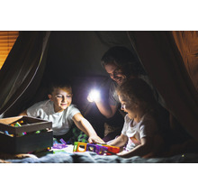 Vater und Kinder spielen mit einer Taschenlampe und Spielzeug in einem Zelt.