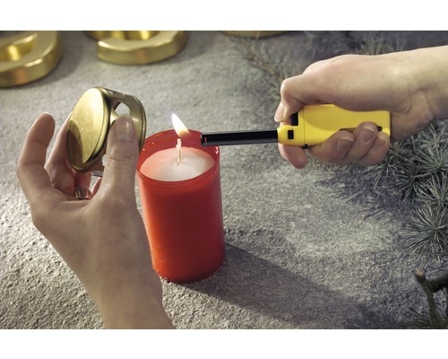 Eine Person zündet eine Kerze mit einem Stabfeuerzeug an. Neben der Kerze liegt ein Kerzendeckel.