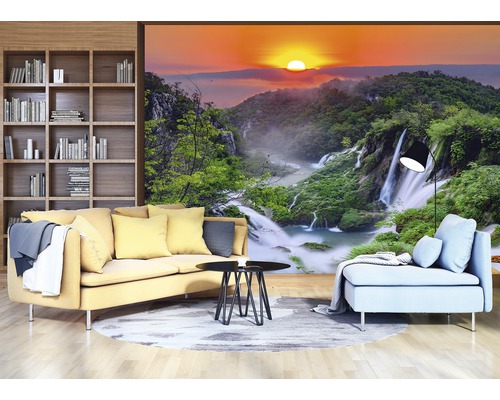 Wohnzimmer mit gelbem Sofa, blauem Sessel und Fototapete mit Wasserfalllandschaft bei Sonnenaufgang
