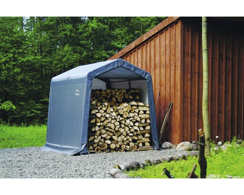 Graue Lagerzelthalle mit Holzstapel im Freien.