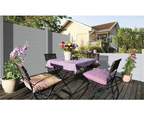 Szene mit einem grauen WPC Zaun, einem Tisch mit Blumen und Stühlen auf einer Terrasse