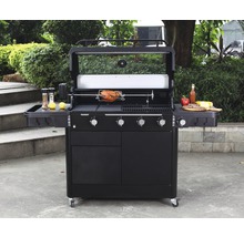Schwarzer Gasgrill mit Drehspieß und Beilagen auf Ablagetischen im Garten.