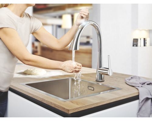 Frau wäscht sich die Hände an einem Küchenspültisch mit Armatur