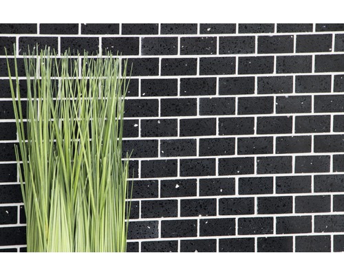 Dekorative grüne Kunstpflanze vor schwarzer Ziegelwand