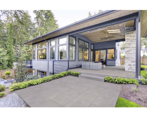 Terrasse mit Betonplatten, Haus mit Holzverkleidung und großen Fenstern