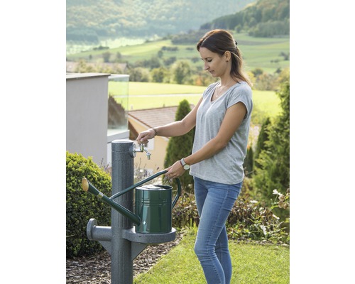Frau befüllt eine Gießkanne an einem Gartenwasserhahn