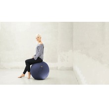 Frau sitzt auf einem blauen Gymnastikball in einem hellen Raum.