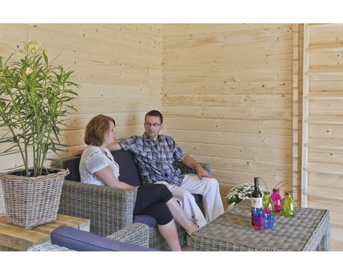 Helle Holzwand mit Paar auf Rattansofa, Tisch mit Getränken und Dekoration sowie Zimmerpflanze im Flechtkorb