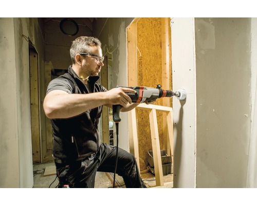 Ein Mann bohrt mit einer Bohrmaschine ein Loch in eine Wand auf einer Baustelle.