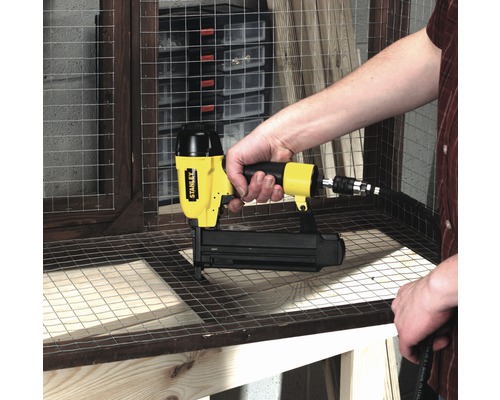 Eine Person verwendet einen Stanley Druckluftnagler auf einem Werkstück mit Drahtgitter.