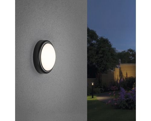 Beleuchtete runde Außenwandleuchte an einer Wand mit Garten im Hintergrund