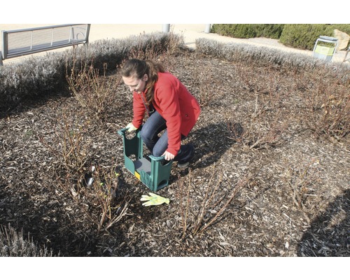 Eine Frau benutzt einen Gartenhocker zur Gartenarbeit in einem Beet.