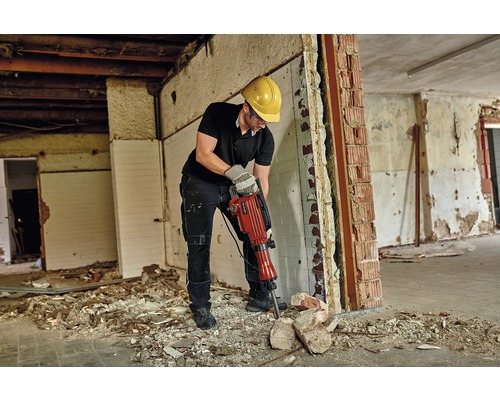 Ein Mann mit Schutzbrille und Schutzhelm arbeitet mit einem Abbruchhammer in einem renovierungsbedürftigen Raum.