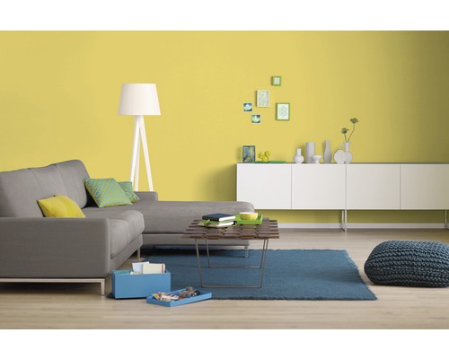 Wohnzimmer mit grauer Couch, Holztisch, blauem Teppich, Stehlampe und gelber Wand