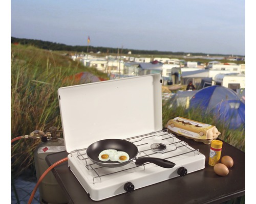 Campingkocher mit Spiegeleiern, Eierkarton und Gewürzen auf einem Tisch im Freien