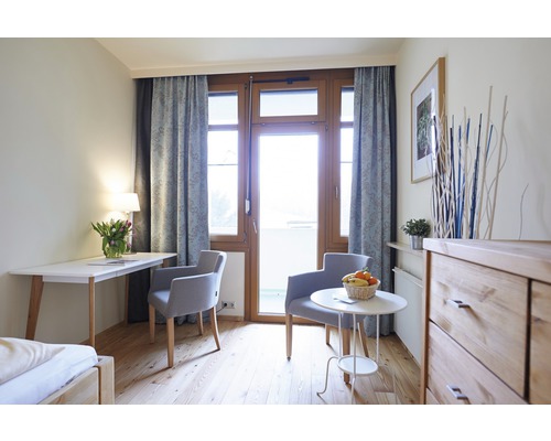 Helles Zimmer mit Schreibtisch, Stühlen, Kommode und Balkontür