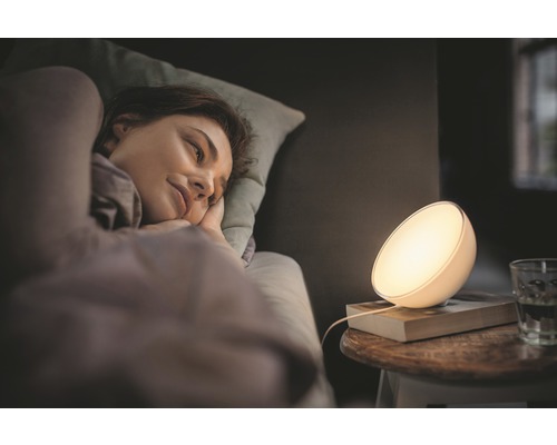 Eine Frau liegt im Bett neben einer Nachttischlampe.