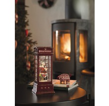 Dekorative Schneekugel in Form einer Telefonzelle mit Weihnachtsmannmotiv und Kamin im Hintergrund.