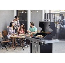 Personen grillen auf einer Terrasse mit einem Gasgrill und genießen eine Mahlzeit am Tisch.