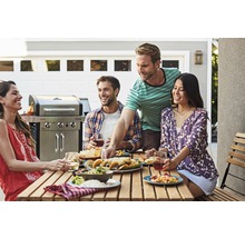 Gruppe von Freunden genießt eine Mahlzeit im Freien mit einem Grill im Hintergrund.