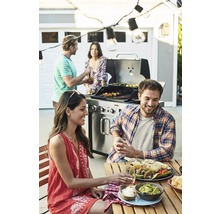 Eine Gruppe von Menschen grillt und isst im Freien, wobei ein Grill, Tacos und Guacamole auf dem Tisch stehen.