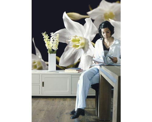 Frau liest Zeitschrift vor einer Fototapete mit Blumenmuster, neben einem Sideboard mit Blumen in einer Vase.