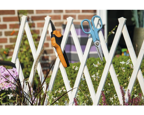 Gartenszene mit Gartenschere und Heckenschere an einem weißen Gartenzaun